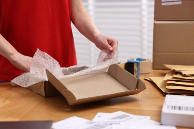 Post office worker packing parcel at wooden table indoors, closeup