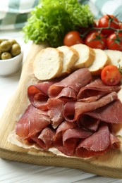 Board with delicious bresaola served with bread and tomato on white wooden table