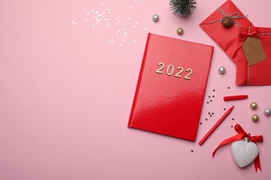 Photo of Red planner and festive decor on pink background, flat lay with space for text. New Year aims