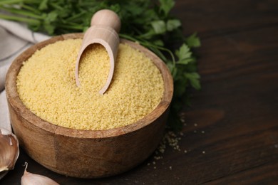 Photo of Bowl and scoop with raw couscous on wooden table, closeup