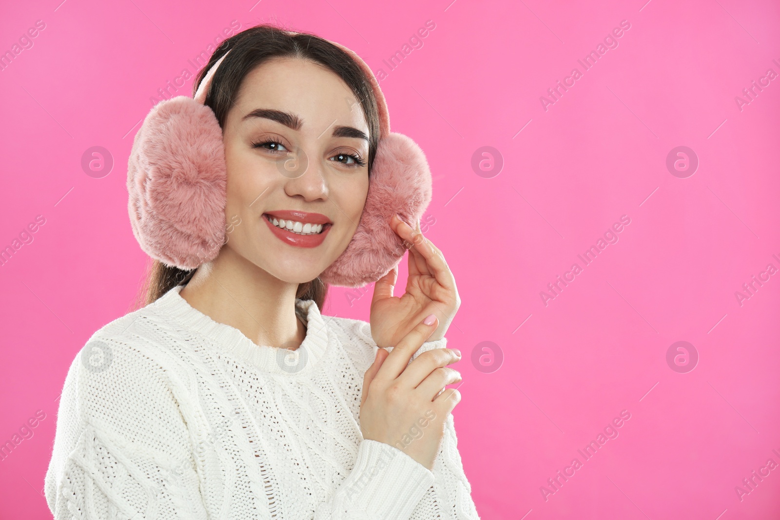 Photo of Beautiful young woman wearing earmuffs on pink background. Space for text