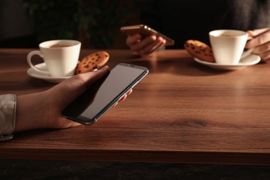 Women using mobile phones at table in cafe, closeup