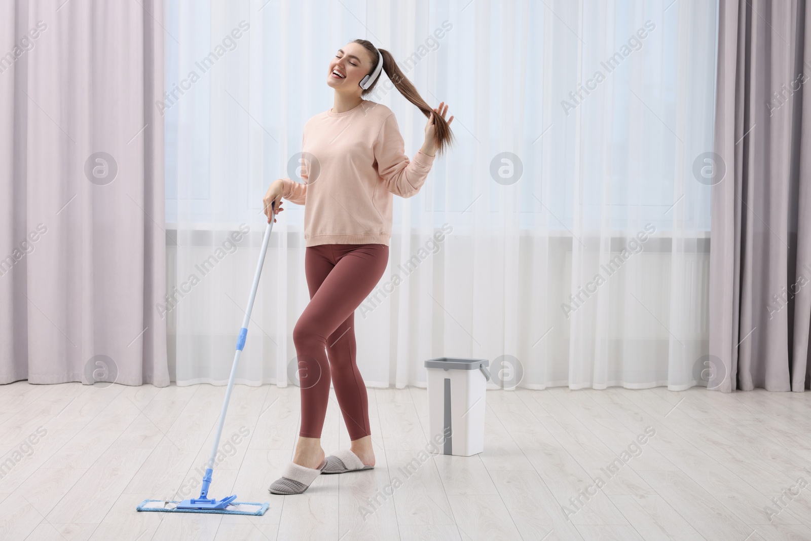 Photo of Enjoying cleaning. Happy woman in headphones listening music and mopping floor indoors. Space for text