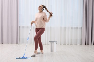 Photo of Enjoying cleaning. Happy woman in headphones listening music and mopping floor indoors. Space for text