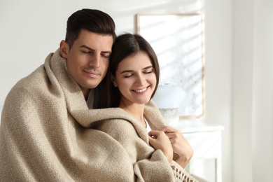 Photo of Happy couple covered with warm beige plaid indoors