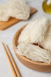Photo of Wooden bowl with uncooked rice noodles on light table, closeup