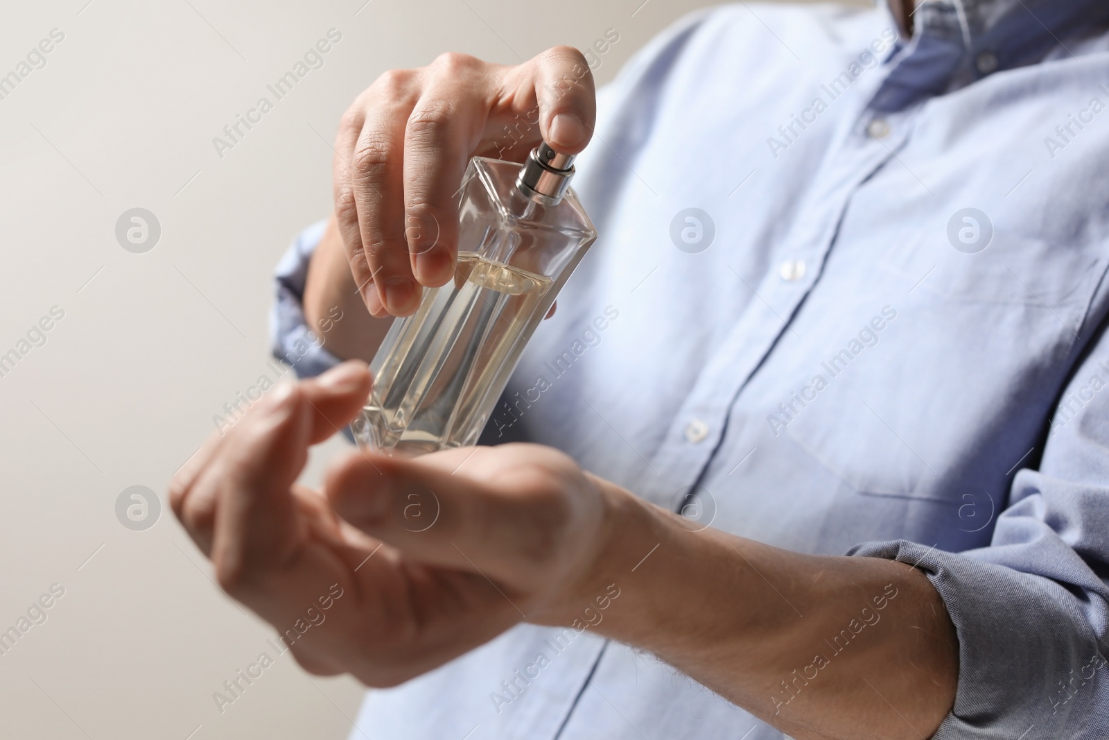 Photo of Man applying perfume on wrist against light background, closeup