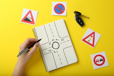 Photo of Woman with workbook for driving lessons and road signs on yellow background, top view. Passing license exam