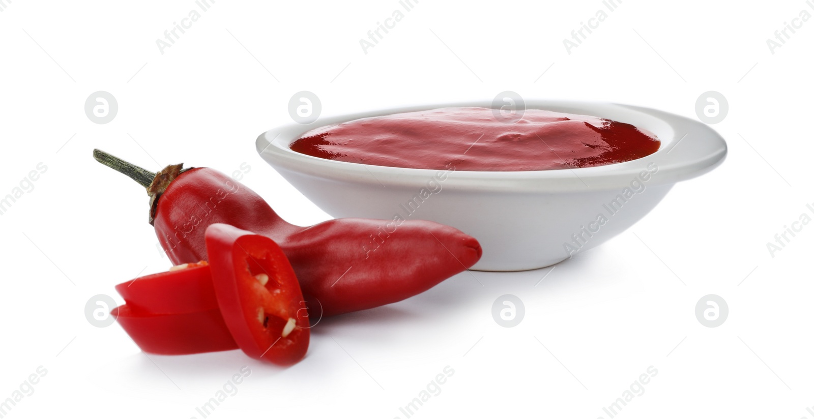 Photo of Bowl with spicy chili sauce and fresh pepper on white background