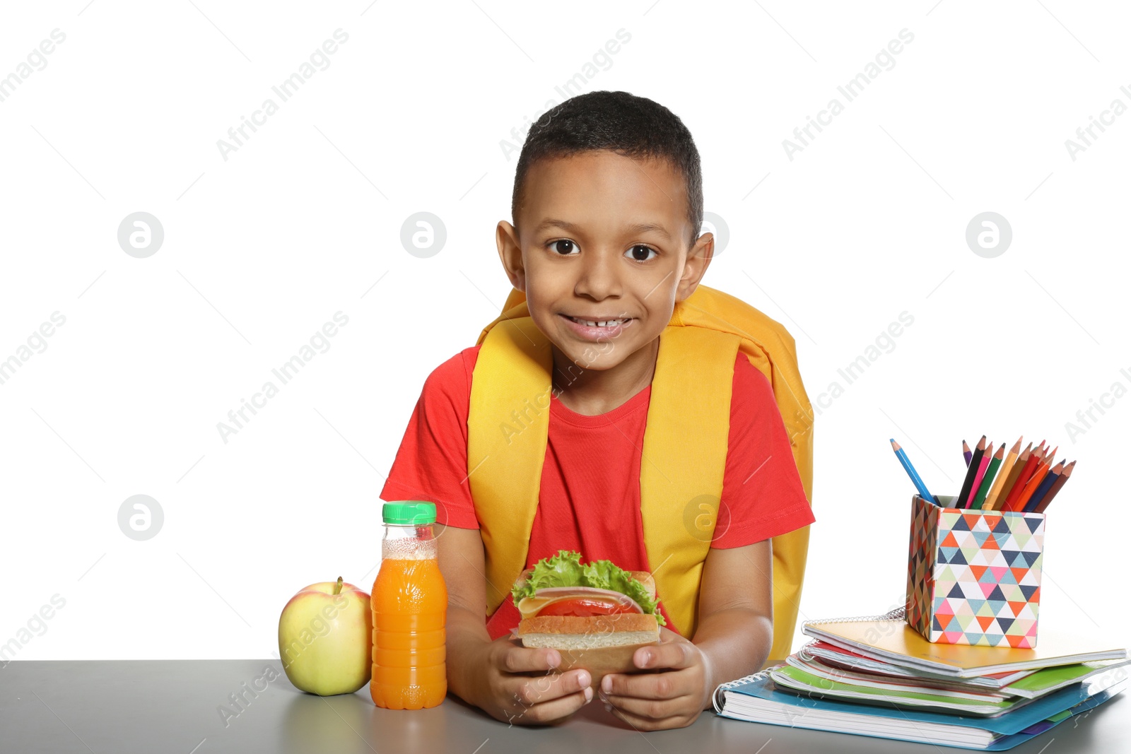 Photo of African-American schoolboy with healthy food and backpack sitting at table on white background