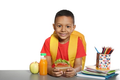 African-American schoolboy with healthy food and backpack sitting at table on white background