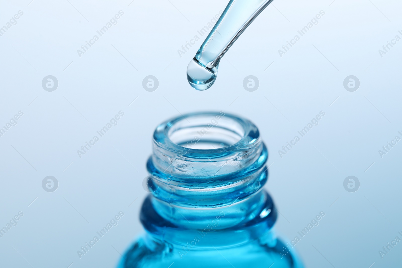 Photo of Dripping liquid from pipette into glass bottle on light blue background, closeup