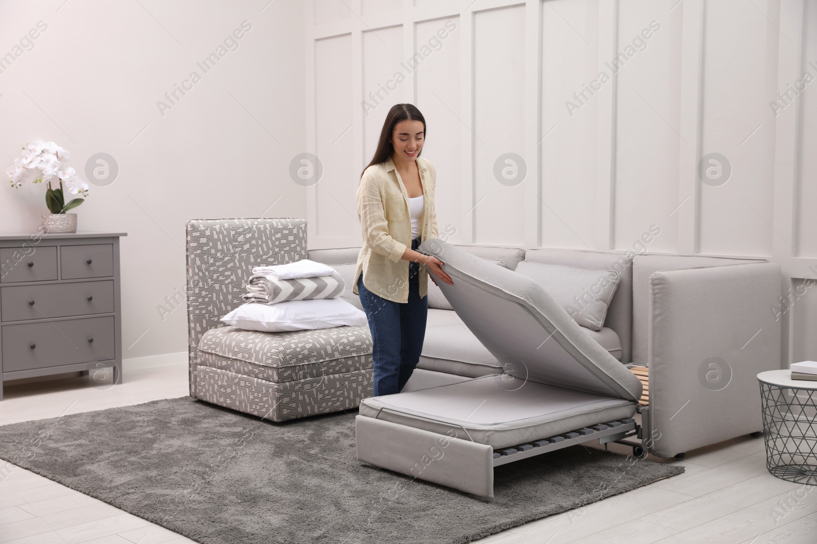 Photo of Woman making sleeping place for guest in living room. Convertible sofa