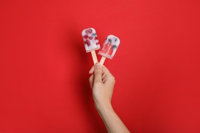 Photo of Woman holding berry popsicles on red background, closeup