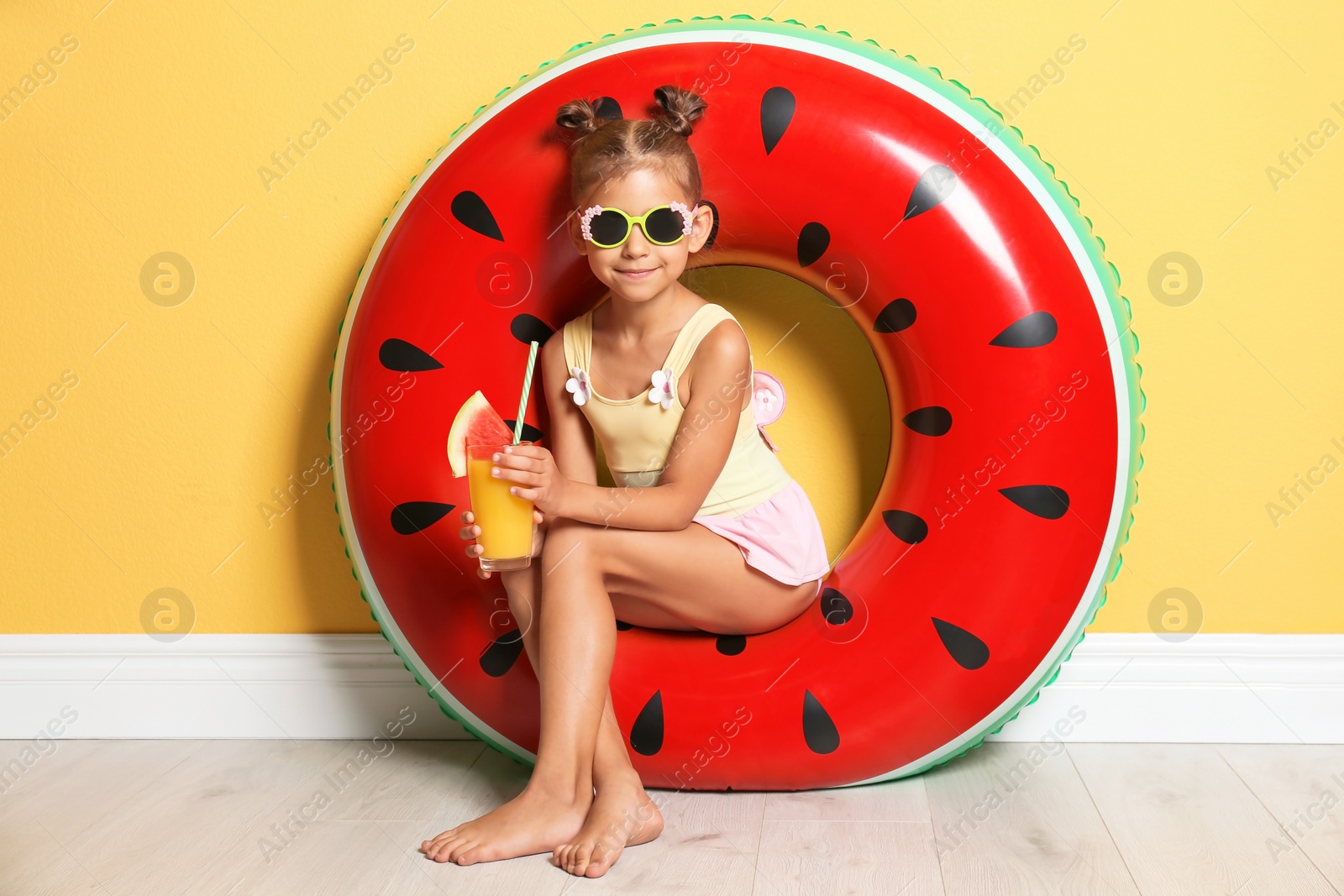 Photo of Cute little girl with inflatable ring and glass of cocktail near color wall