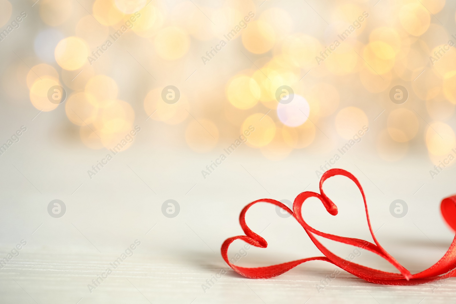 Photo of Two hearts made of red ribbon on table against blurred lights, space for text. St. Valentine's day card