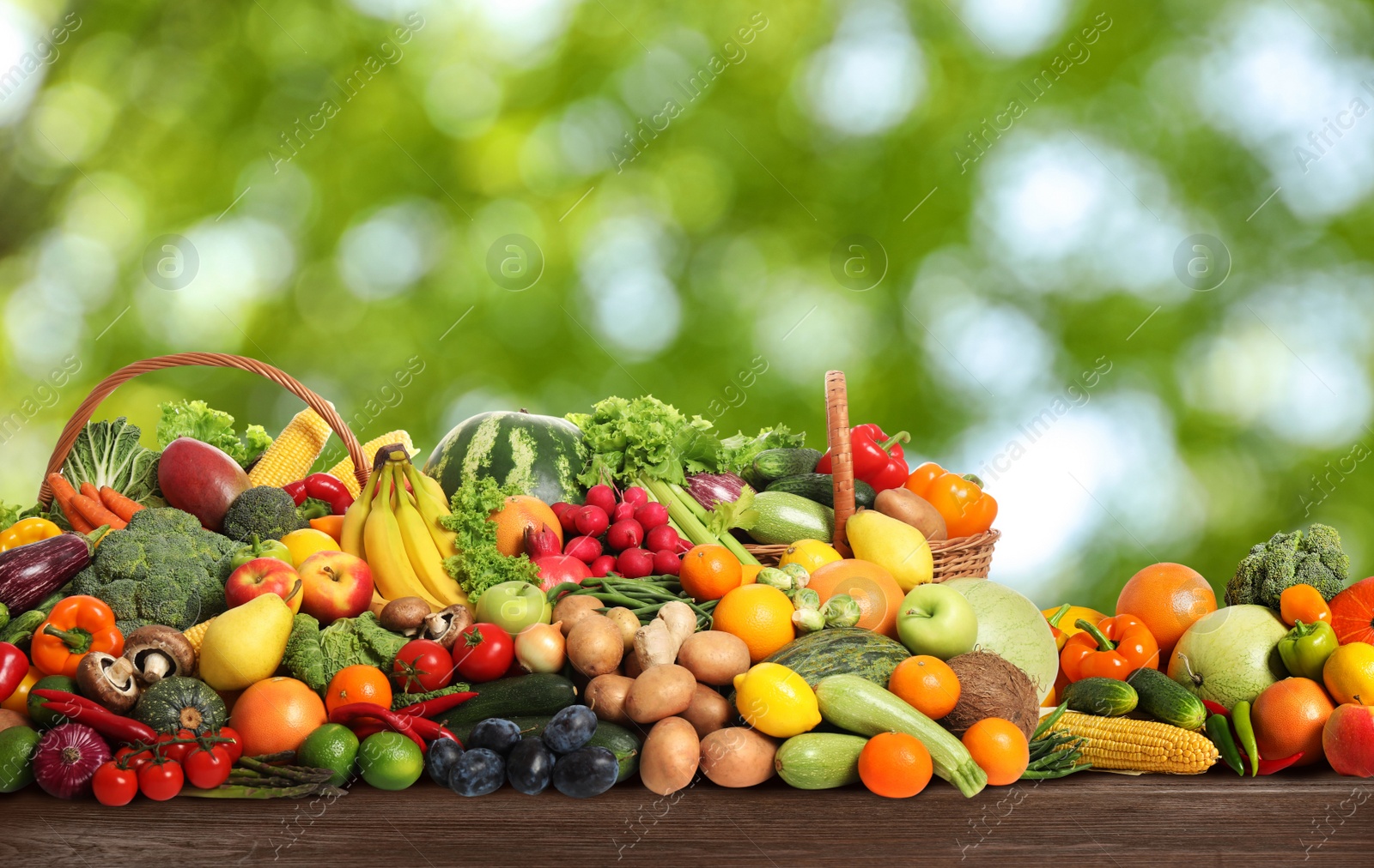 Image of Assortment of fresh organic vegetables and fruits on wooden table against blurred green background