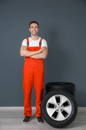 Photo of Young mechanic in uniform with car tires near dark wall