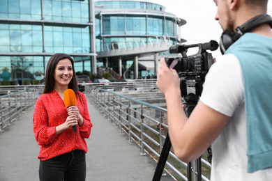 Young journalist and video operator working on city street