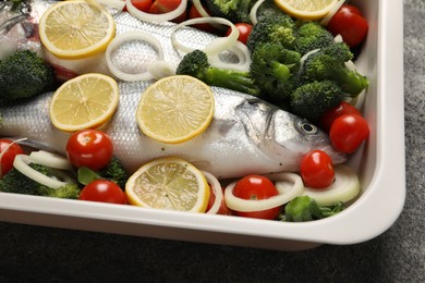 Raw fish with vegetables and lemon in baking dish on grey table