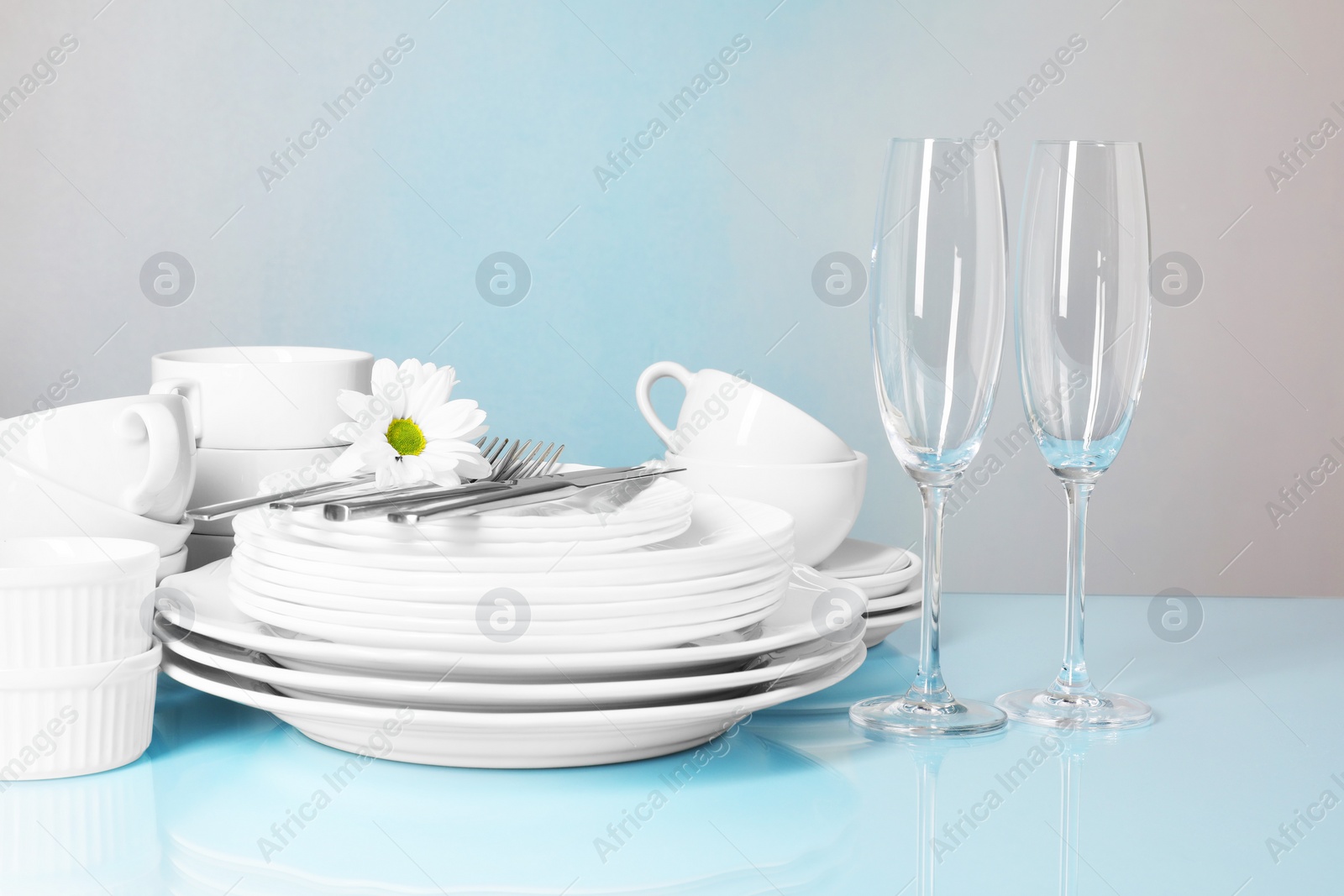 Photo of Set of clean dishes, glasses and cutlery on light blue table