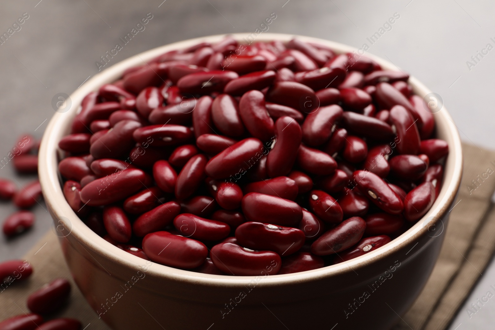 Photo of Raw red kidney beans in bowl and napkin on table, closeup