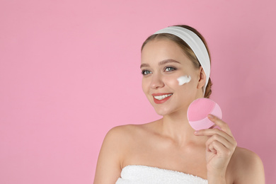 Young woman washing face with brush and cleansing foam on pink background, space for text. Cosmetic product