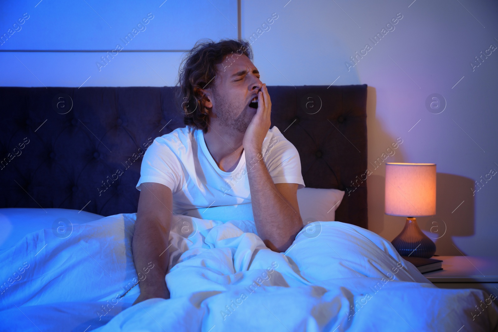 Photo of Sleepy young man yawning in dark room at night. Bedtime