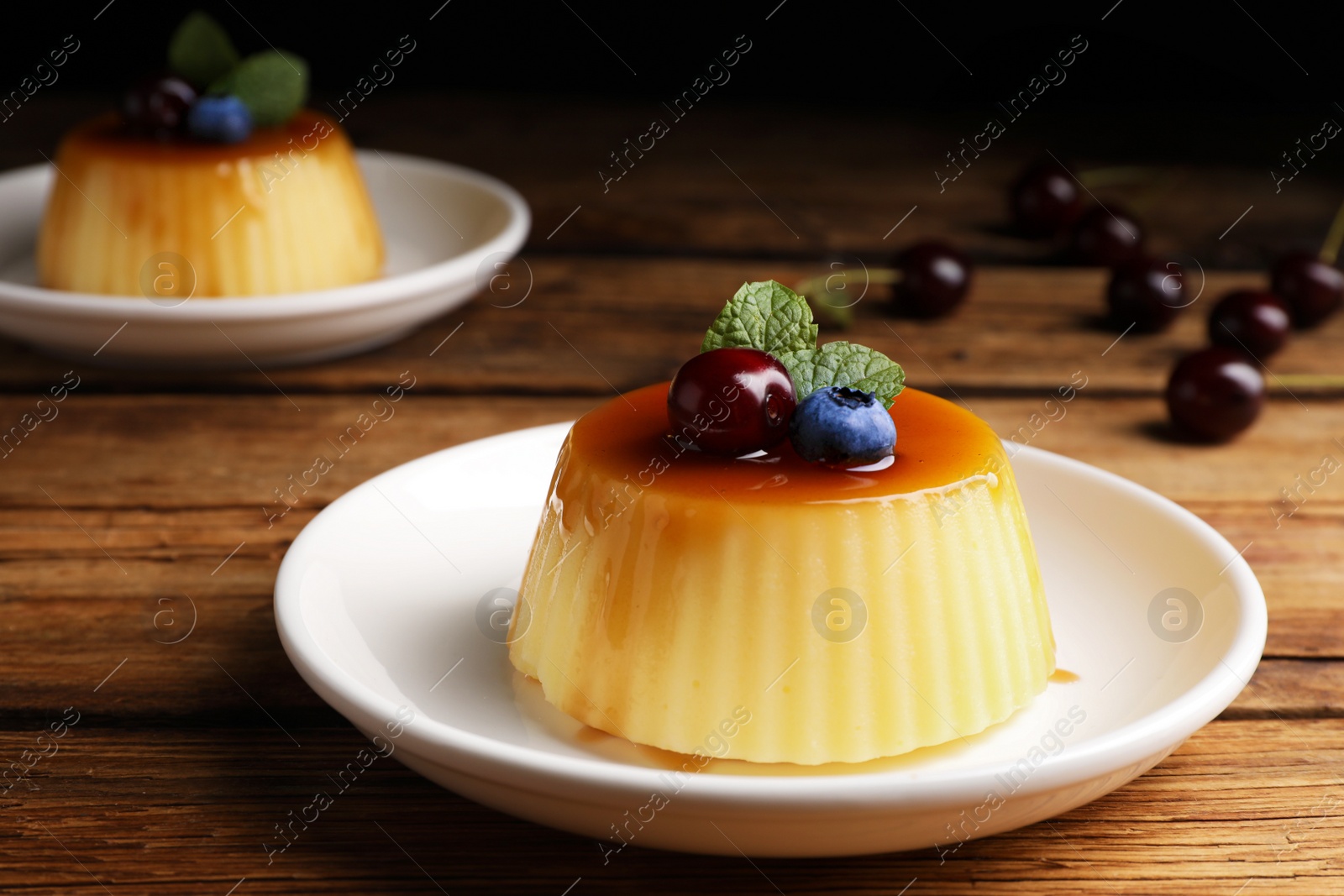Photo of Plate of delicious caramel pudding with blueberry, cherry and mint on wooden table