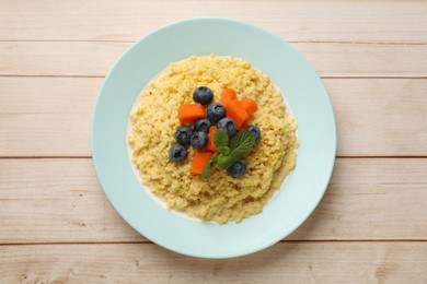 Plate with tasty millet porridge, blueberries, pumpkin and mint on light wooden table, top view