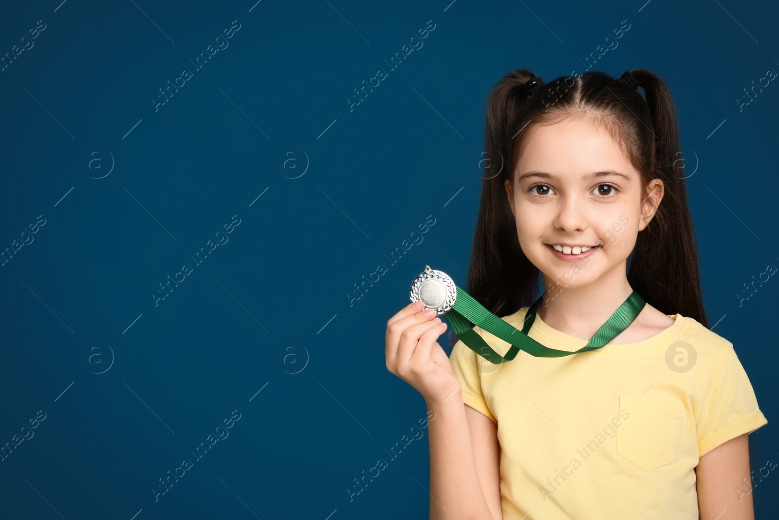 Photo of Happy girl with golden medal on dark blue background. Space for text