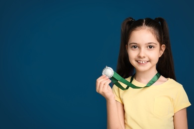 Photo of Happy girl with golden medal on dark blue background. Space for text