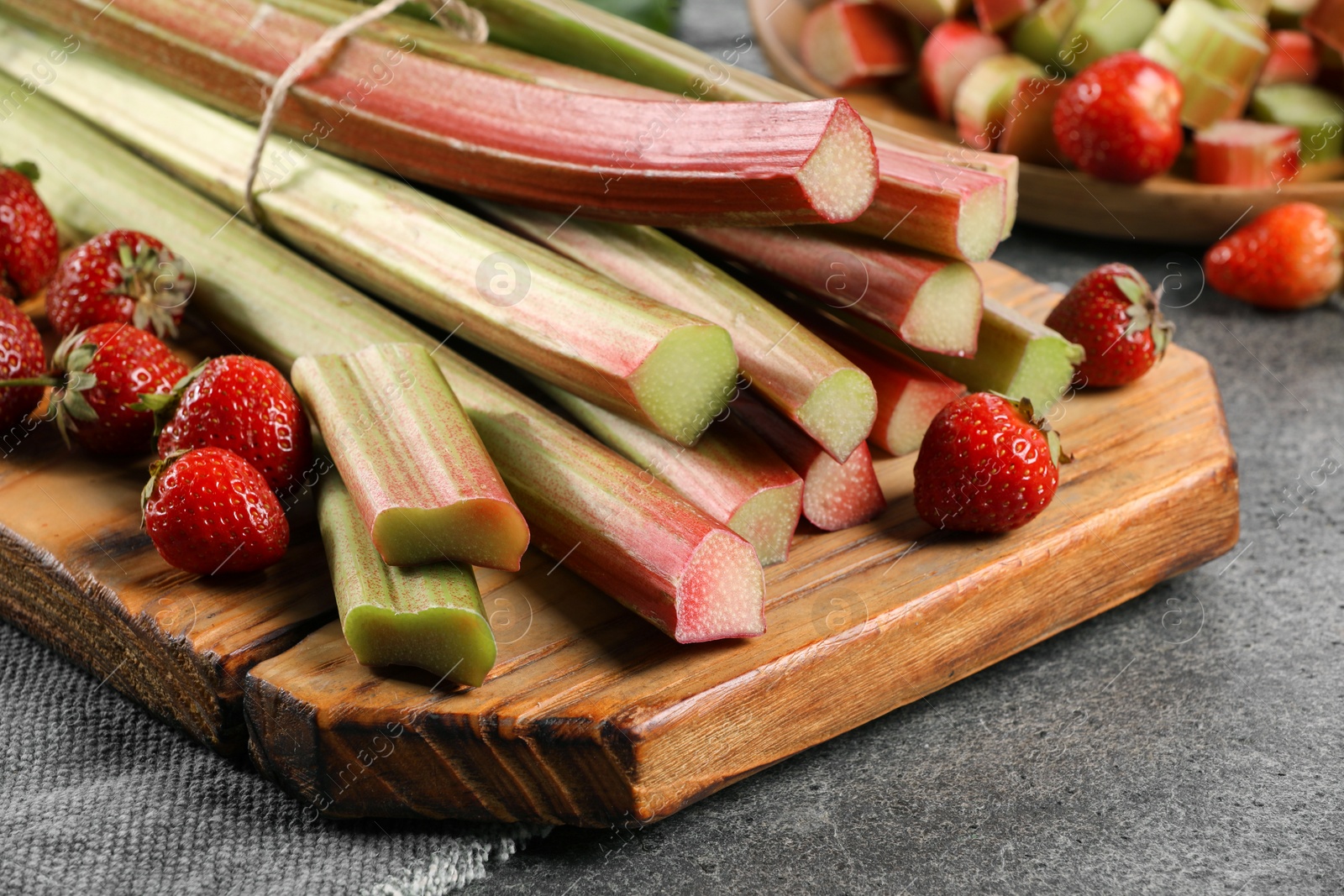 Photo of Fresh ripe rhubarb stalks and strawberries on grey table, closeup