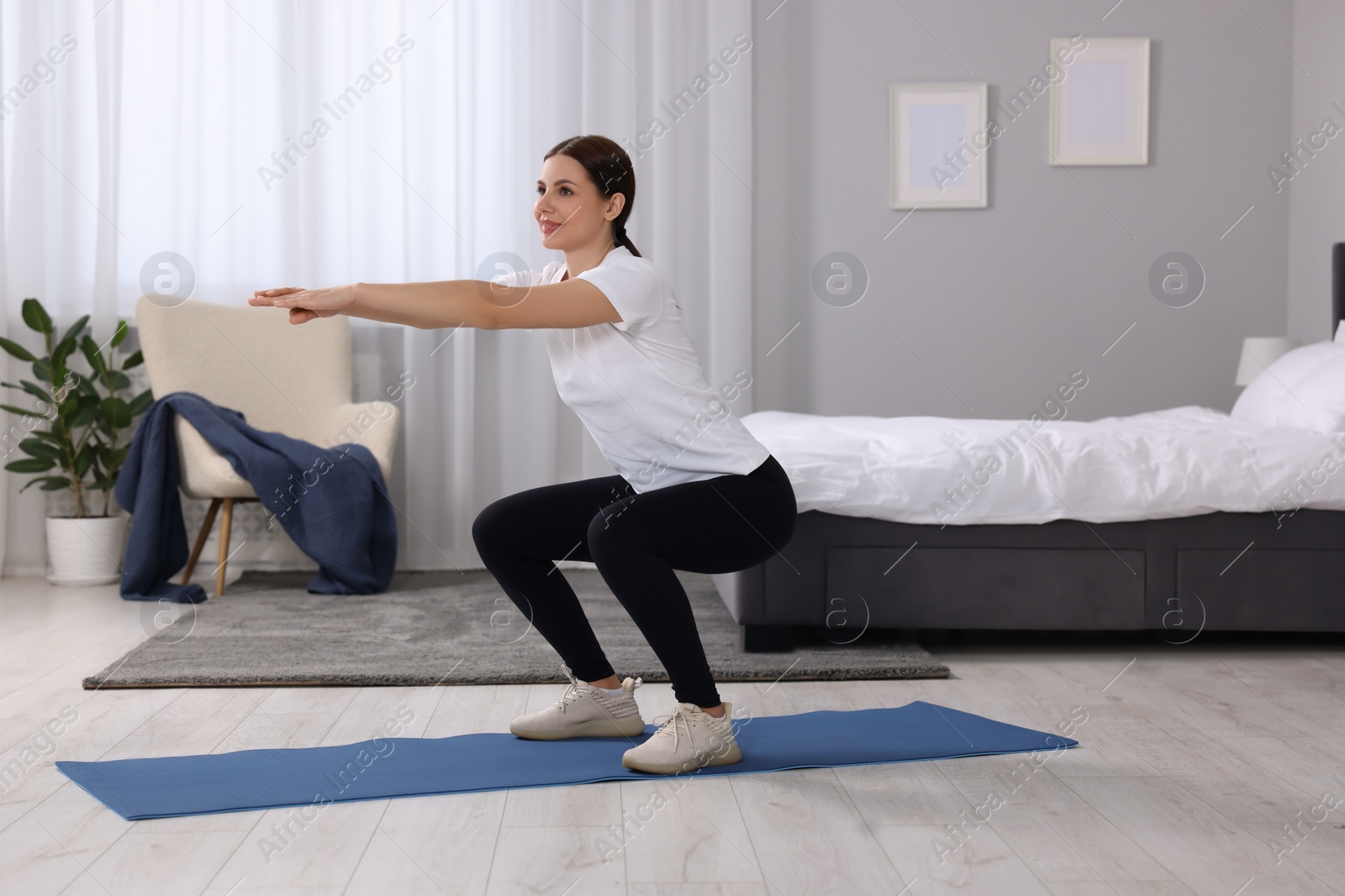 Photo of Morning exercise. Happy woman squatting at home, space for text