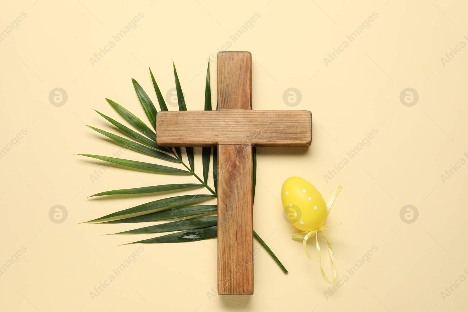 Photo of Wooden cross, painted Easter egg and palm leaf on beige background, top view