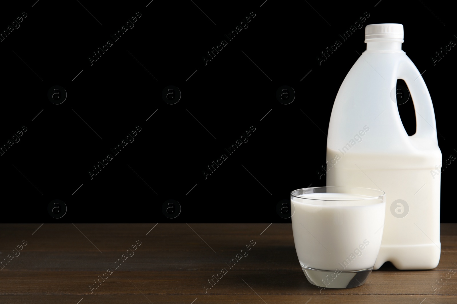 Photo of Gallon bottle and glass of milk on wooden table. Space for text