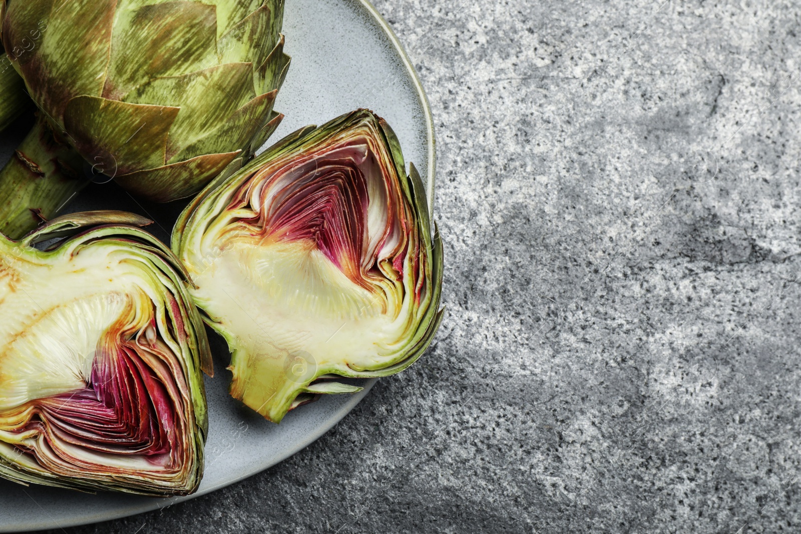 Photo of Cut and whole fresh raw artichokes on grey table, top view. Space for text