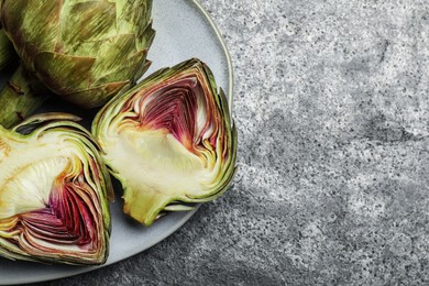 Cut and whole fresh raw artichokes on grey table, top view. Space for text