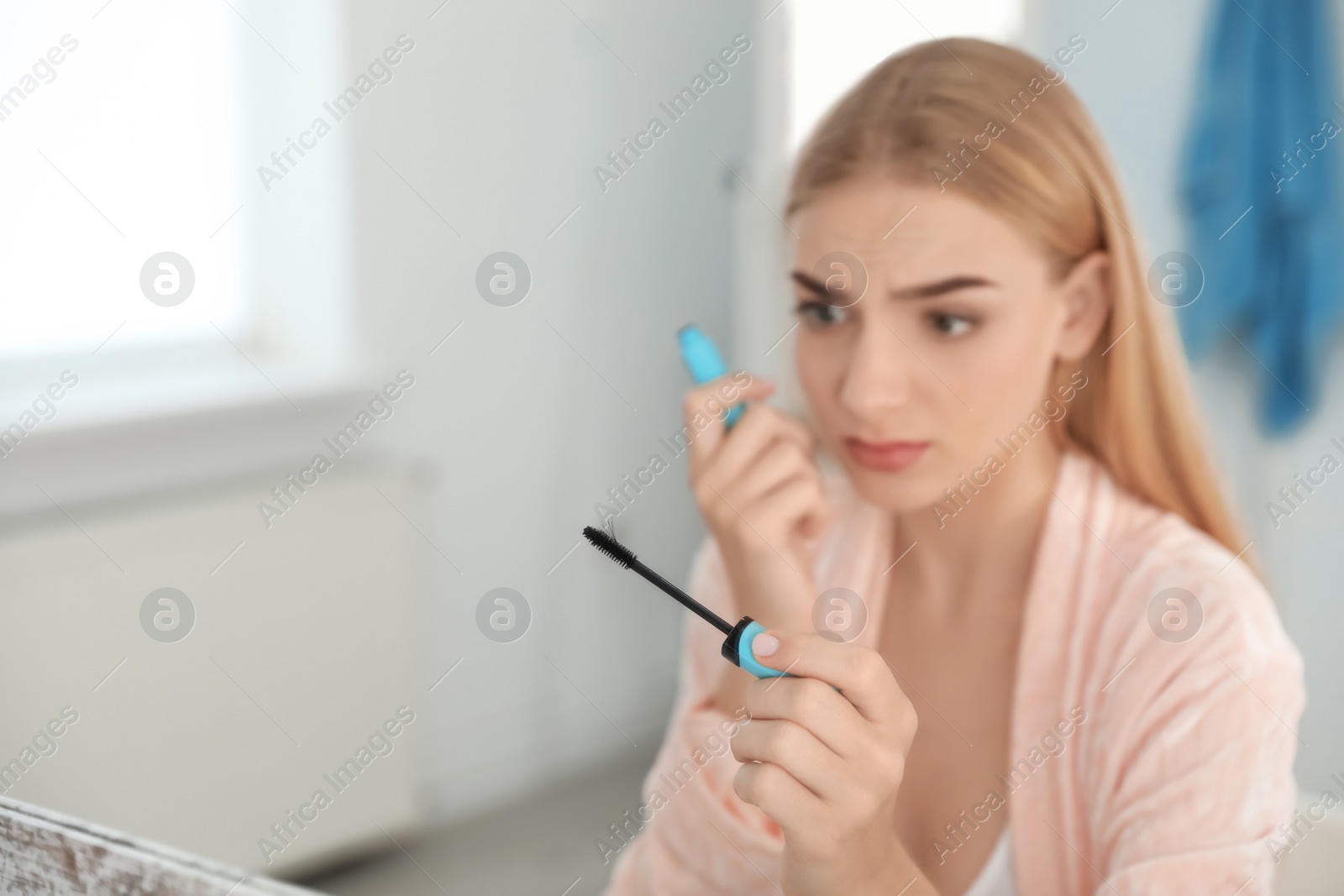 Photo of Young woman holding mascara brush with fallen eyelashes indoors