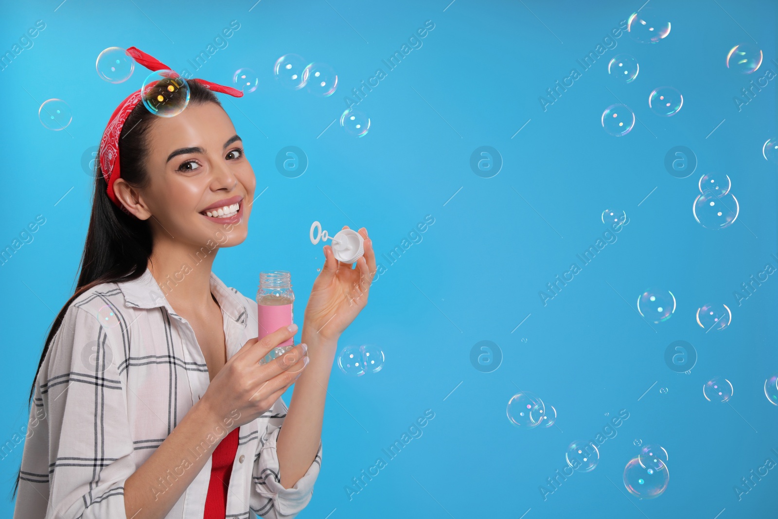 Photo of Young woman blowing soap bubbles on light blue background, space for text