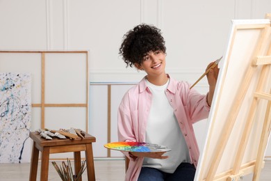 Young woman painting on easel with canvas in studio