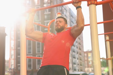 Photo of Man training on horizontal bar at outdoor gym on sunny day