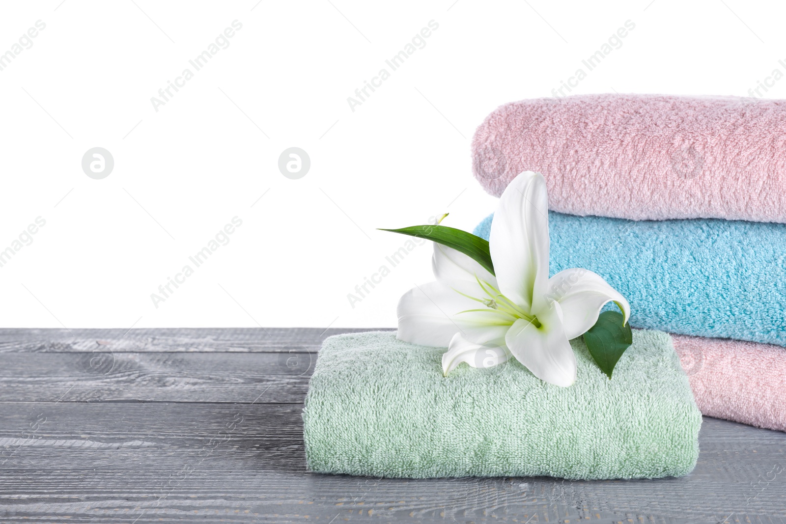 Photo of Fresh towels and lily flower on grey wooden table against white background. Space for text