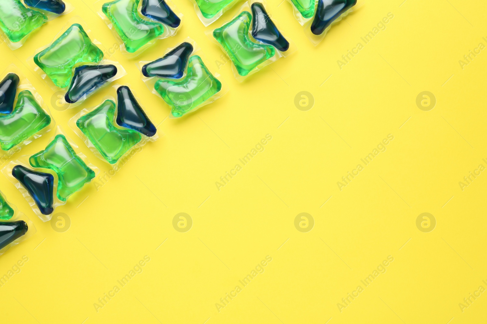 Photo of Laundry capsules on yellow background, flat lay. Space for text