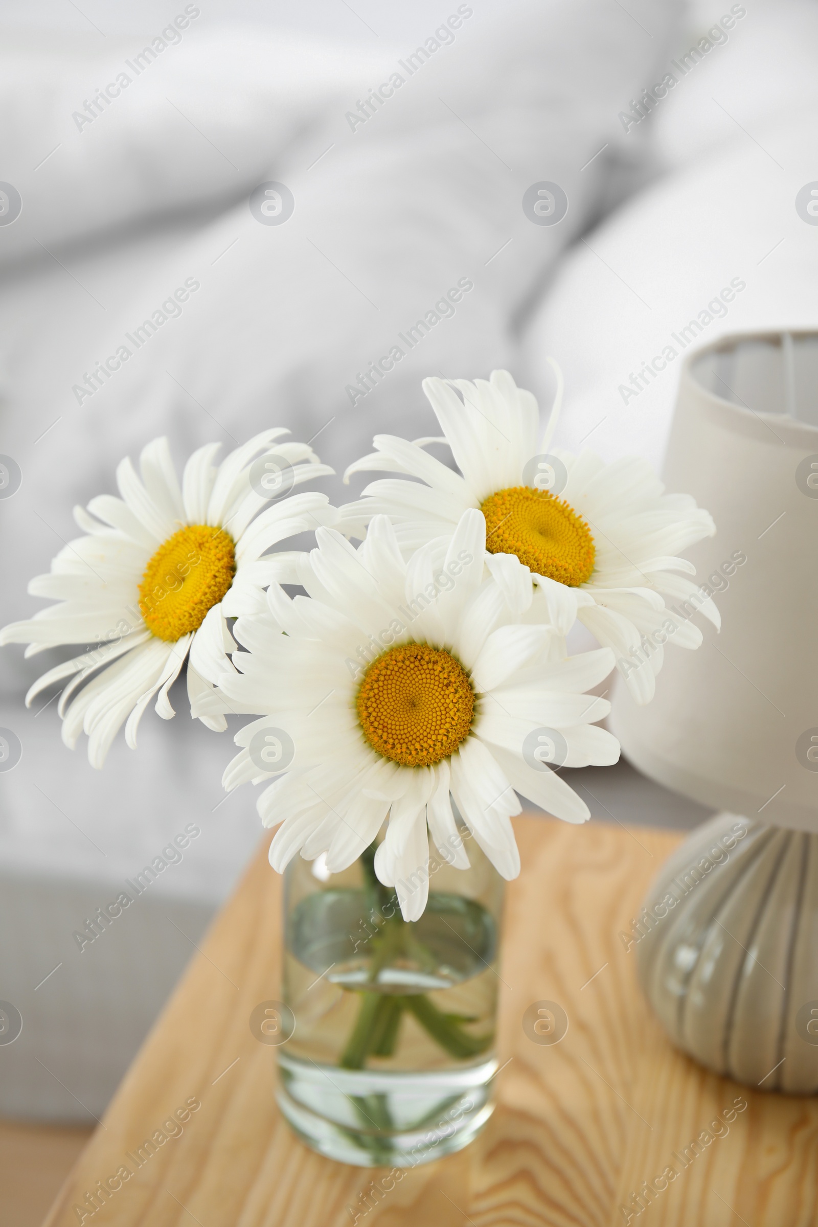 Photo of Bouquet of beautiful daisy flowers and lamp on nightstand in bedroom