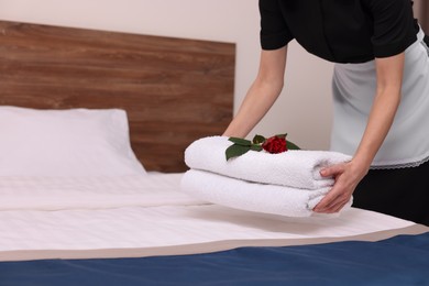 Photo of Chambermaid putting fresh towels with flower on bed in hotel room, closeup