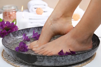 Photo of Woman pouring water onto her feet in bowl on floor, closeup. Spa treatment