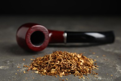 Photo of Pile of tobacco and smoking pipe on grey table against dark background