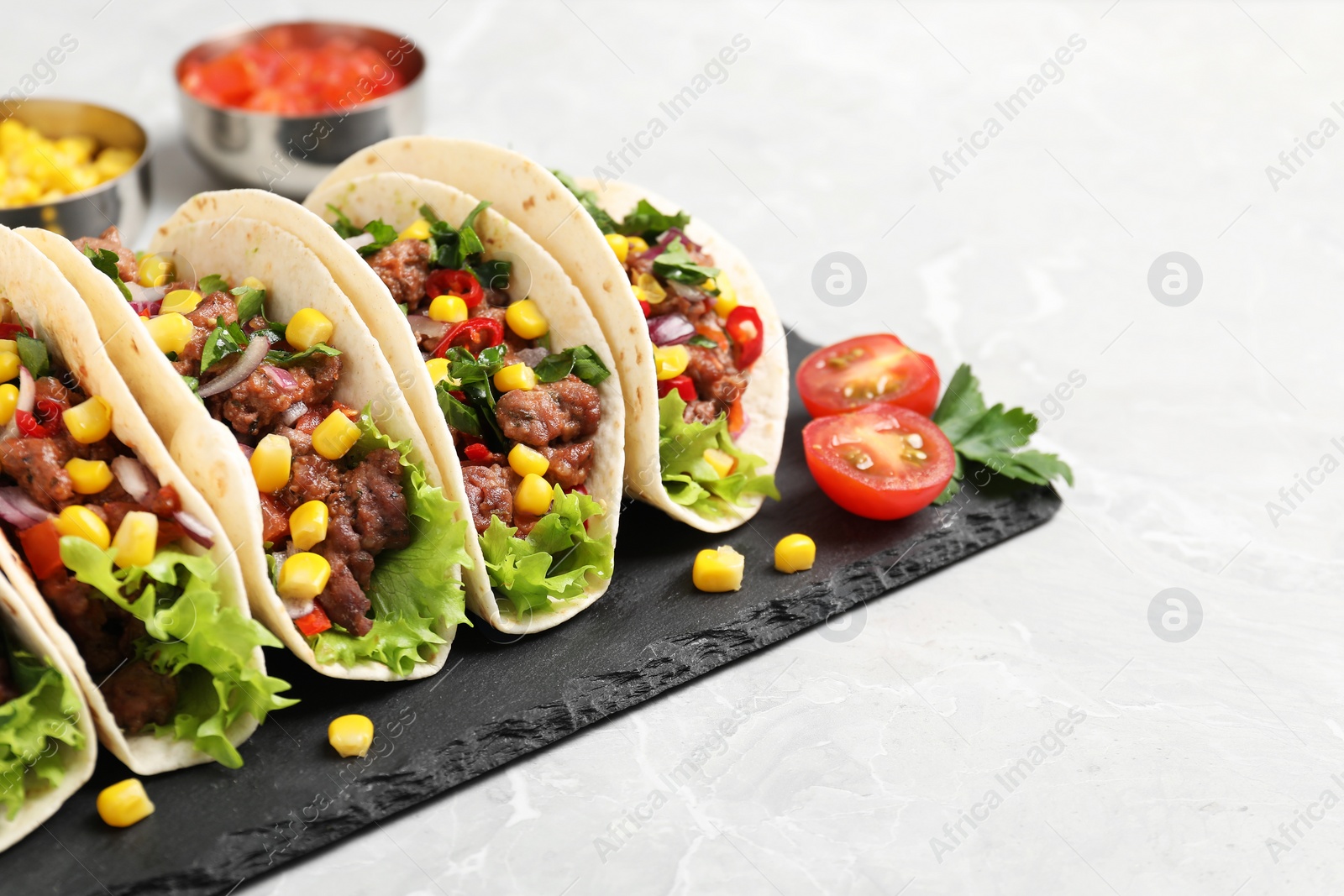 Photo of Delicious tacos with meat and vegetables on light gray marble table, closeup