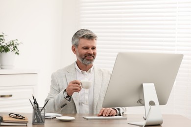 Professional accountant with cup of coffee working at wooden desk in office